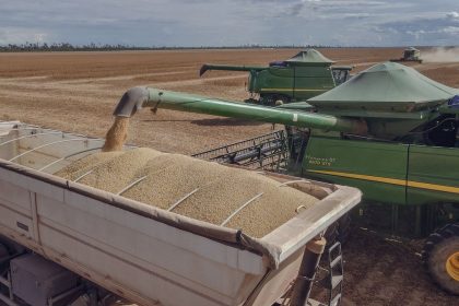 Colheitadeiras carregam soja em um caminhão durante a colheita em um campo agrícola no Brasil.
