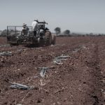 Agricultores trabalham em um trator preparando o solo de uma área rural para o próximo plantio.